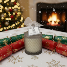 Candle with a decorative bow in front of a Christmas tree and fireplace