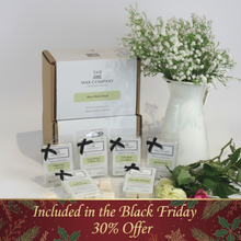 A collection of wax melt cubes from The Little Wax Company, displayed in front of a box with a 6 pack indication. The cubes are labeled with different fragrance names and are presented in clear packaging with black bows.