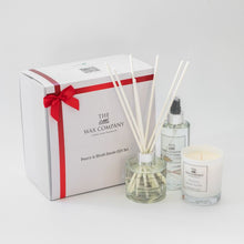 A luxury gift box set containing a white classic candle, a reed diffuser, and a room spray, all tied with a red ribbon.