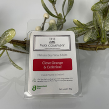 Pack of The Little Wax Company clove orange & cedarleaf wax melts with decorative greenery in the background.