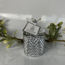 Silver textured candle with decorative tag on a white background with greenery