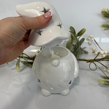 White ceramic piggy bank with star design on lid, held by a hand against a white background with decorative elements.