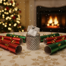 Decorative cracker with a small ornament on a table in front of a Christmas tree and fireplace.
