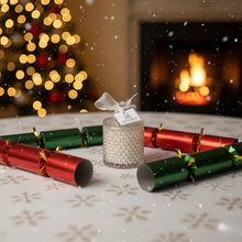 Decorative gift with a bow and tag in front of Christmas crackers and a fireplace with lights.