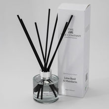 A clear glass reed diffuser with black reeds and a white label, alongside its packaging box with the brand name and fragrance details.